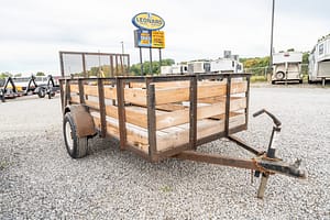 Image 0 for SKU 47326 – Leonard Truck and Trailer, Inc Wooden stake-bed trailer on a gravel lot, with a Leonard Truck & Trailer sign in the background.