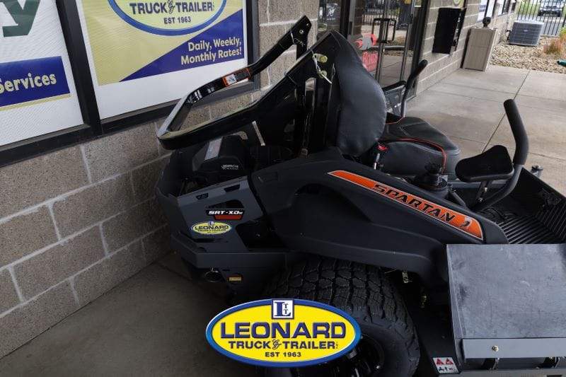 Black Spartan riding lawn mower with orange stripe, parked beside a storefront with Leonard Truck & Trailer logo on the ground.
