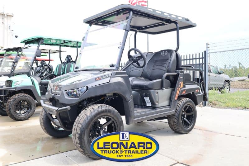 Black off-road utility golf cart with roof on display at Leonard Truck & Trailer lot, front view highlighting large tires and dashboard.