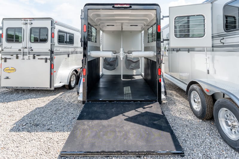 Open horse trailer with ramp down; empty interior showing two padded stalls and divider rails.