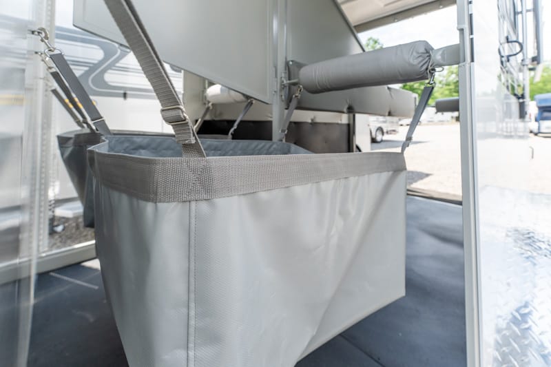 Gray fabric storage tote hanging from straps under the underside of an RV/trailer.