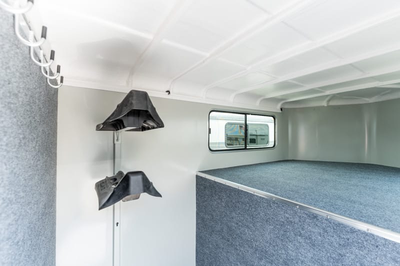 Interior of a small sleeper compartment with a raised blue-carpeted bed and window on the far wall, plus wall hooks on the left.