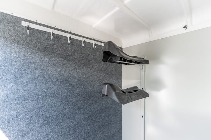 Interior of a small trailer showing two black plastic footrests mounted on a peg rail on a dark grey wall in the cargo area.