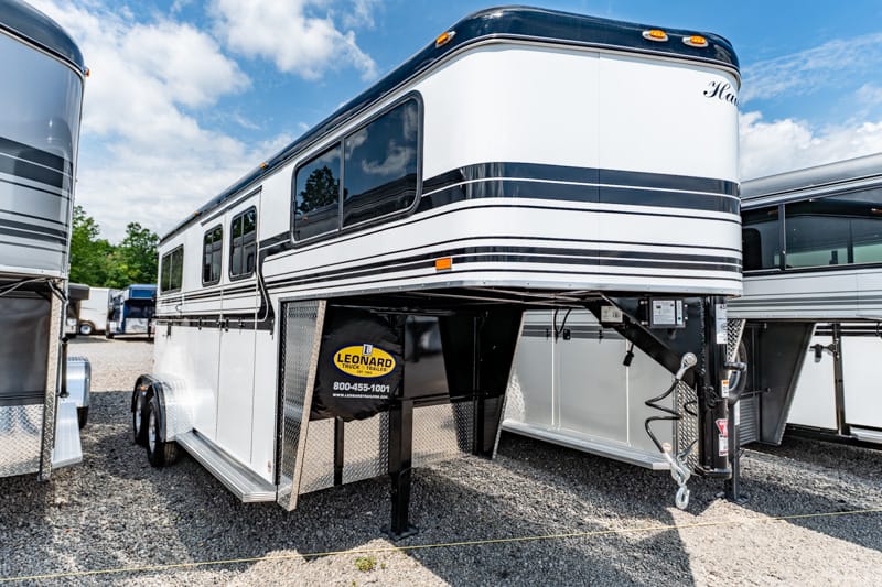 White fifth-wheel recreational trailer with living quarters, shown on a gravel dealership lot with other trailers nearby.
