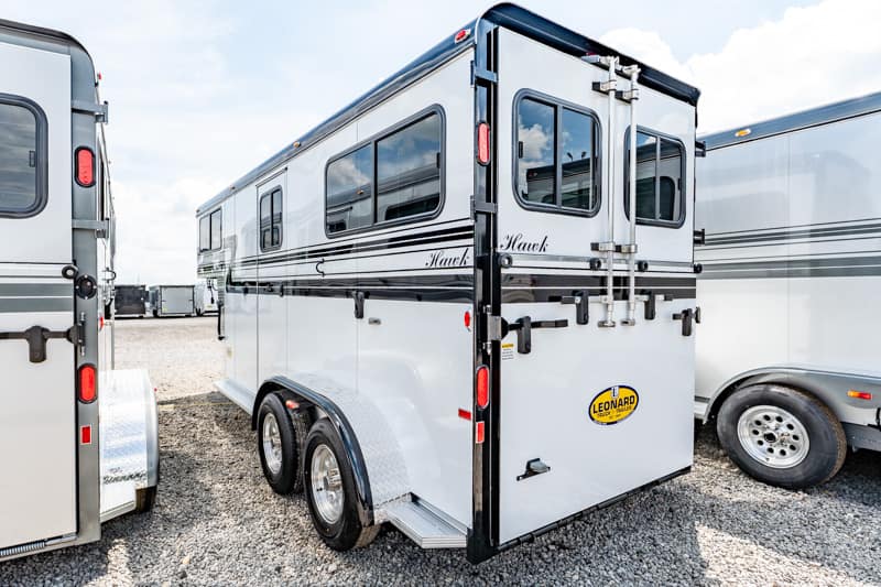 White two-axle horse trailer with black trim, dual rear doors, parked on gravel.