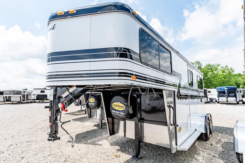 Large white fifth-wheel RV trailer with black stripes parked on a gravel lot, hitch and storage compartments visible in the foreground.