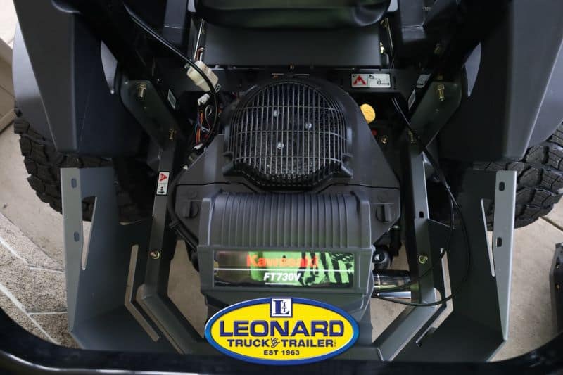 Close-up of the front engine compartment of a Kawasaki riding lawn mower, showing the air intake grille and the Kawasaki FT730V label, with a Leonard Truck & Trailer emblem at the bottom.