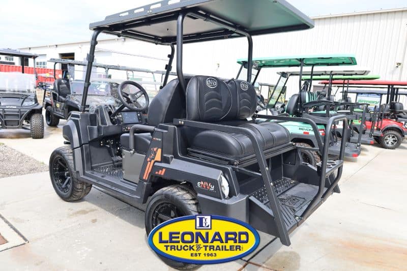 Dark gray multi-passenger golf cart with a roof, parked on a dealership lot beside other carts; Leonard Truck & Trailer logo in the foreground.