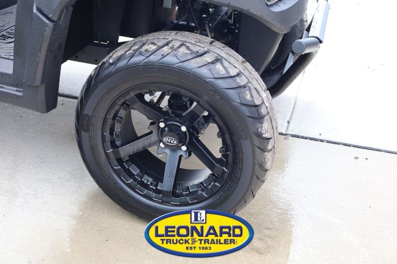 Close-up of a black multi-spoke wheel and tire on a vehicle, wet concrete beneath, Leonard Truck & Trailer logo visible at the bottom.