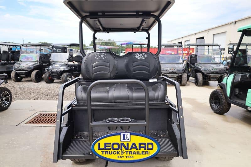 Rear view of a black golf cart with two seats and a canopy, parked at a Leonard Truck & Trailer dealership lot, logo visible on the rear plate