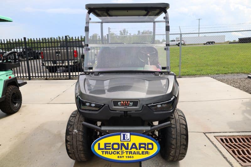 Front view of a dark gray utility golf cart with windshield, parked on concrete; Leonard Truck & Trailer sign in the foreground."